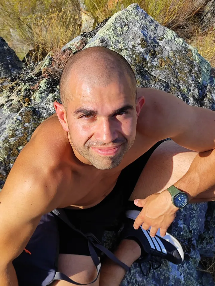 Ismael sitting against a lichen-covered boulder on a hillside in late afternoon sun, looking up at the camera.